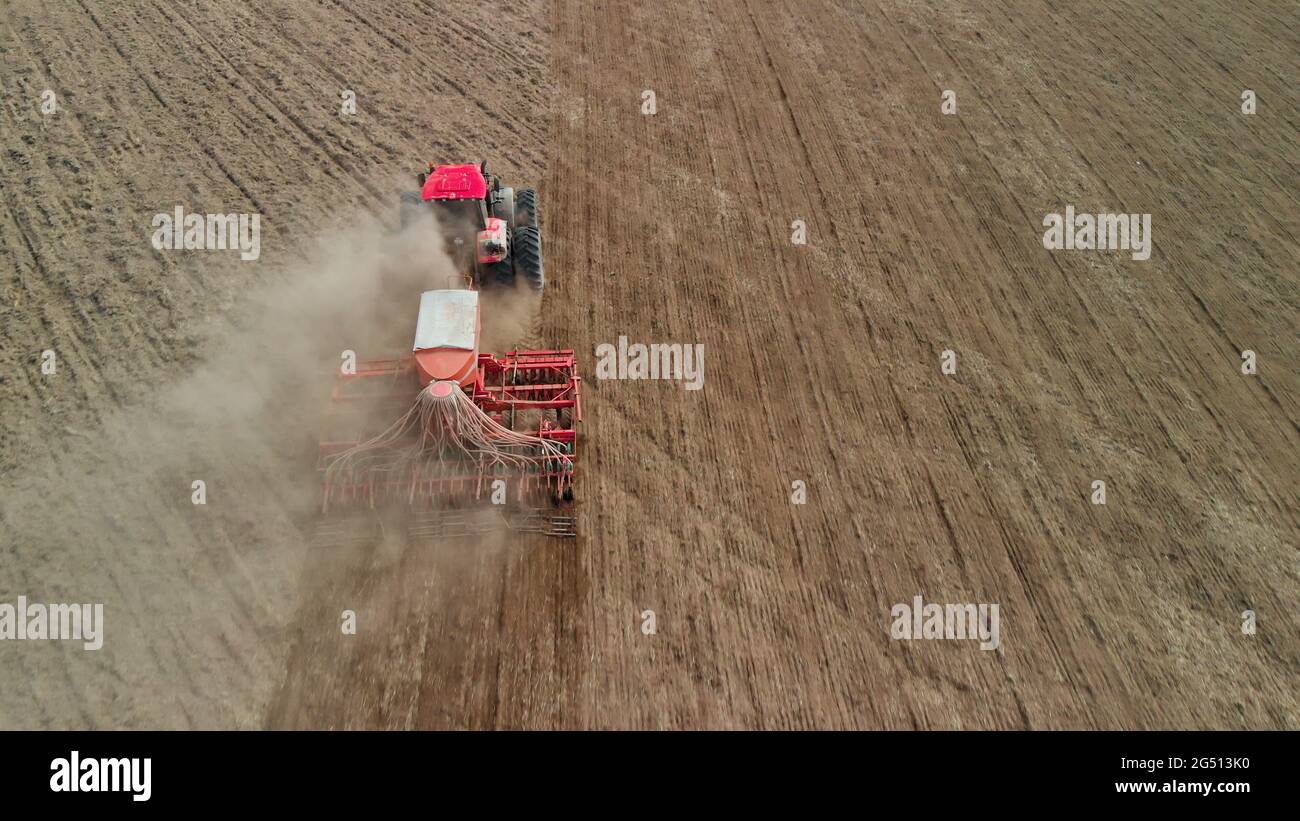 Tractor with a unit processes dusty soil on the prairie. Farmer sows in arid, lifeless steppes. Concept of risky agribusiness. Aerial view Stock Photo