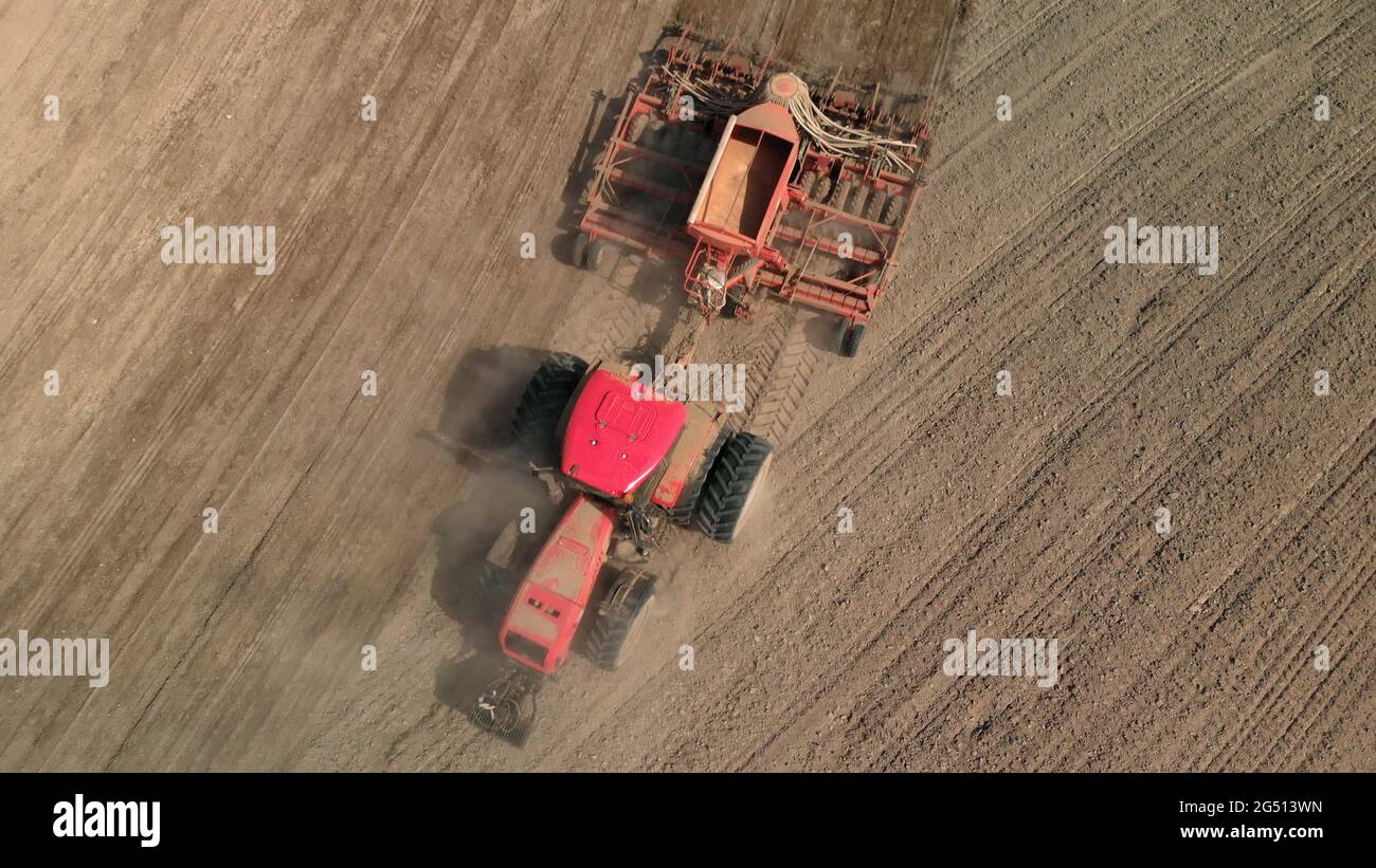 Tractor with a unit processes dusty soil on the prairie. Farmer sows in arid, lifeless steppes. Concept of risky agribusiness. Aerial view Stock Photo