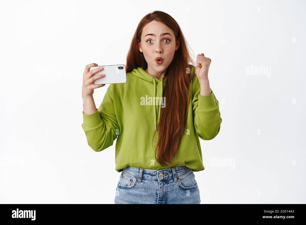 Excited teen redhead girl winning on mobile phone game, watching video on  smartphone and celebrating, make fist pump and triumphing, white background  Stock Photo - Alamy