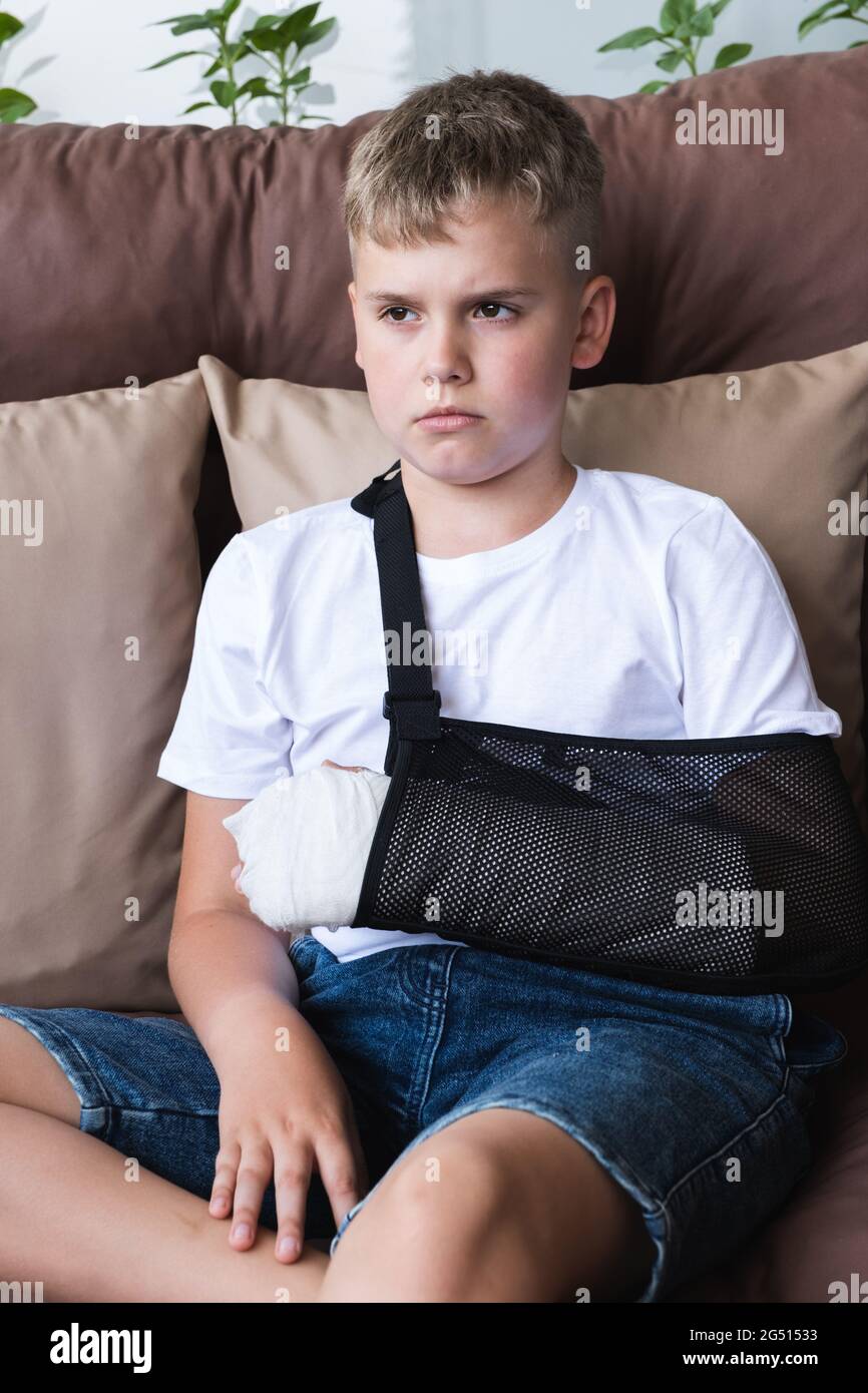 Sad boy with broken arm in cast sits at home on balcony. Stock Photo