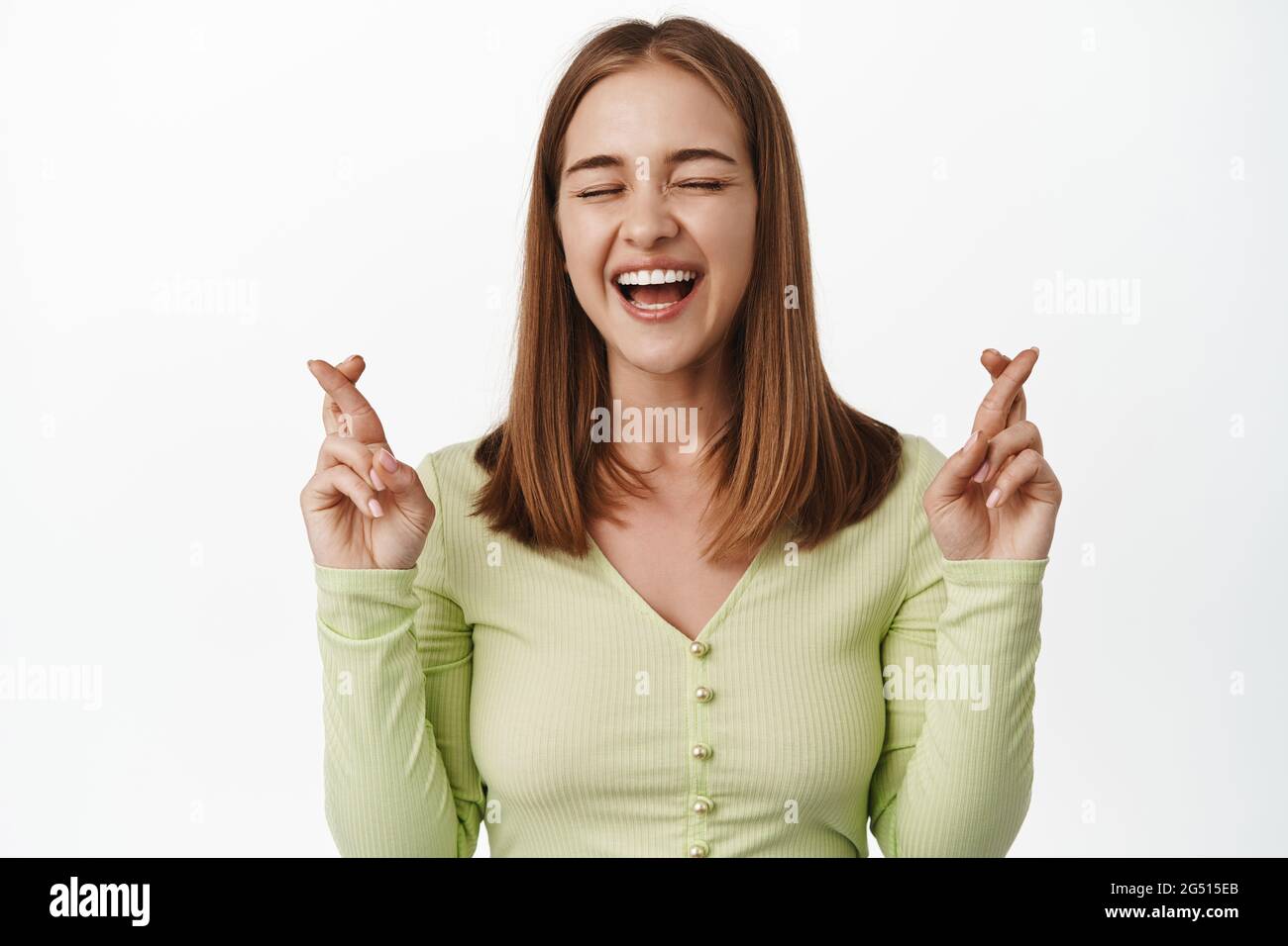 Cheerful blond girl laughs and makes wish, cross fingers optimistic, praying for good luck, wishing to pass exams, anticipating big news, white Stock Photo