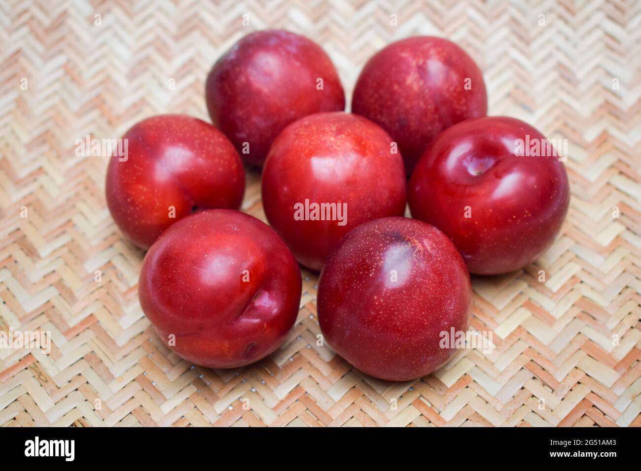 Plums fruits fresh organic bright red maroon color. On wicker bamboo