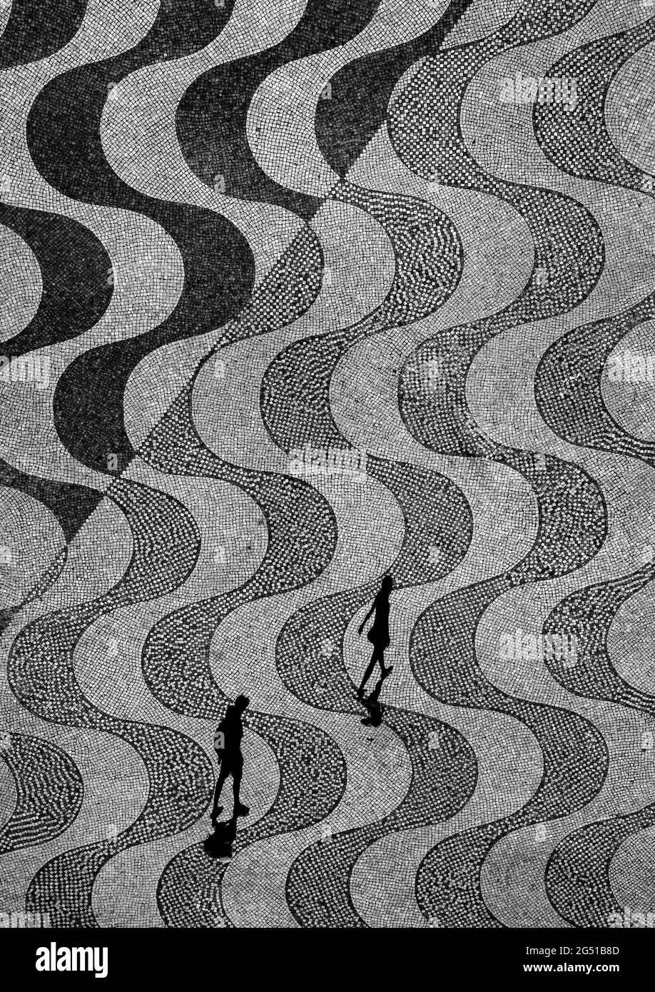 A man walks behind a woman in Belém, a district in Lisbon, Portugal, under the discoveries monument, by the Tagus river. Stock Photo