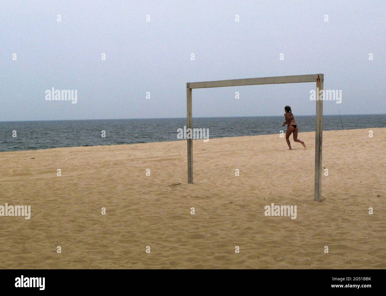 A woman running towards the water, framed by a football goal, at the beach in Leblon. Rio de Janeiro, Brazil. Stock Photo