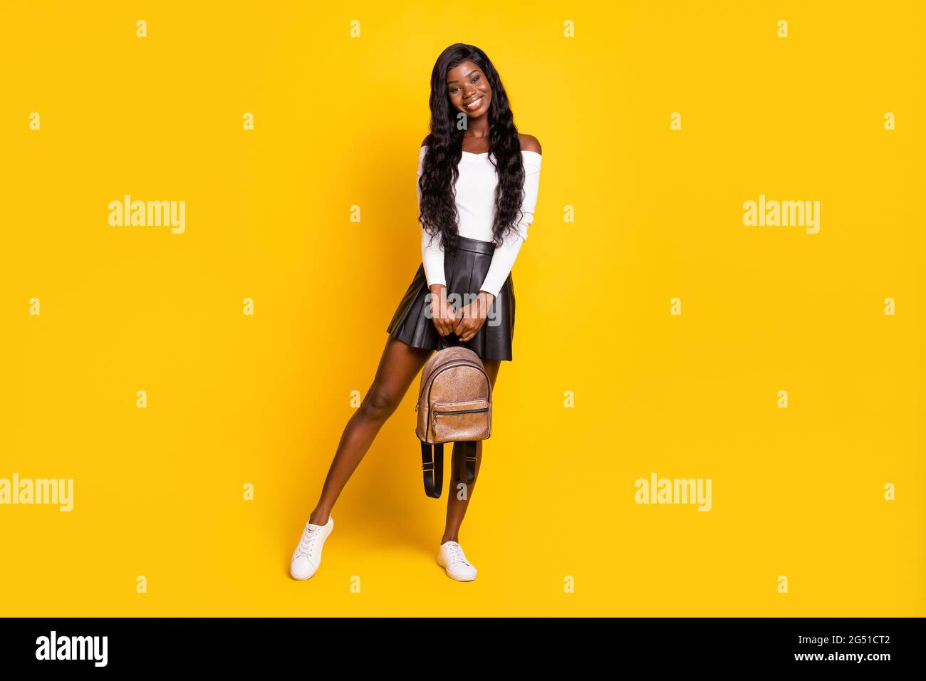 Full length body size photo black skinned brunette smiling holding rucksack wearing short skirt isolated on vibrant yellow color background Stock Photo