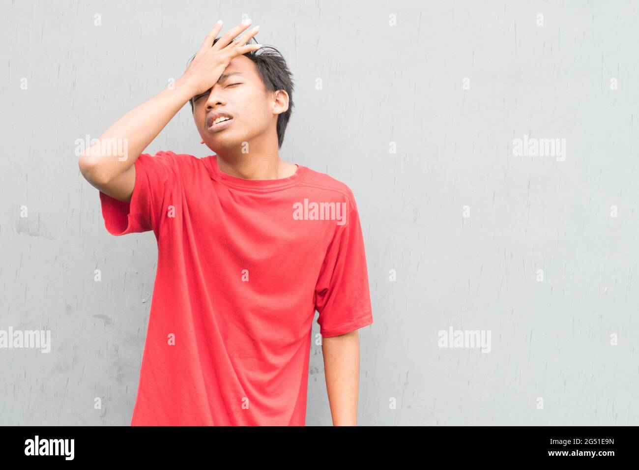 Indonesian guy wearing a red tshirt suffering from a headache Stock
