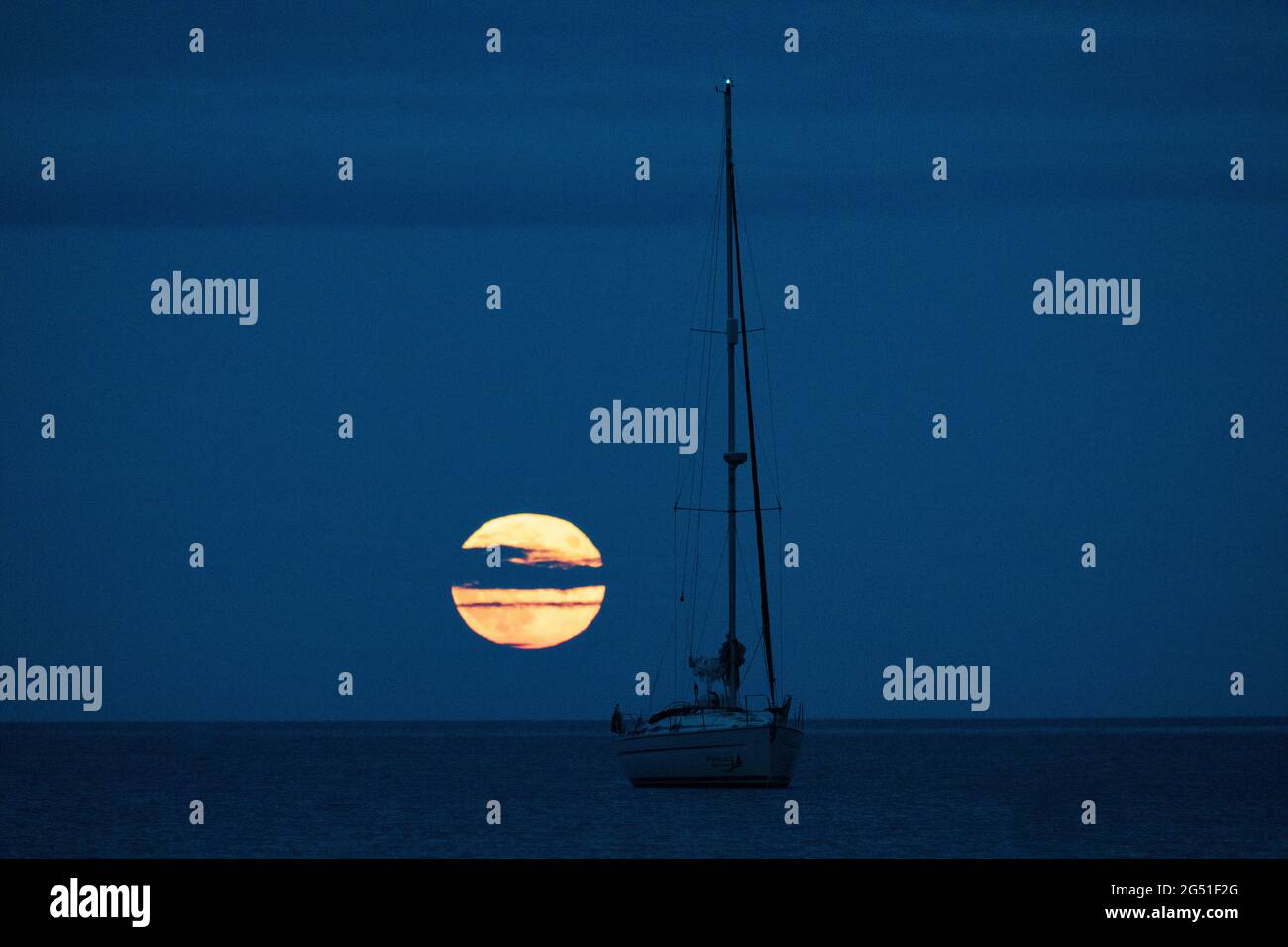 Cawsand Bay, Cornwall, UK. UK Weather: 24th June 2021. The Strawberry Full Super Moon rising on the horizon at Cawsand Bay with clearing sky to view the spectacle © DGDImages/AlamyNews Stock Photo