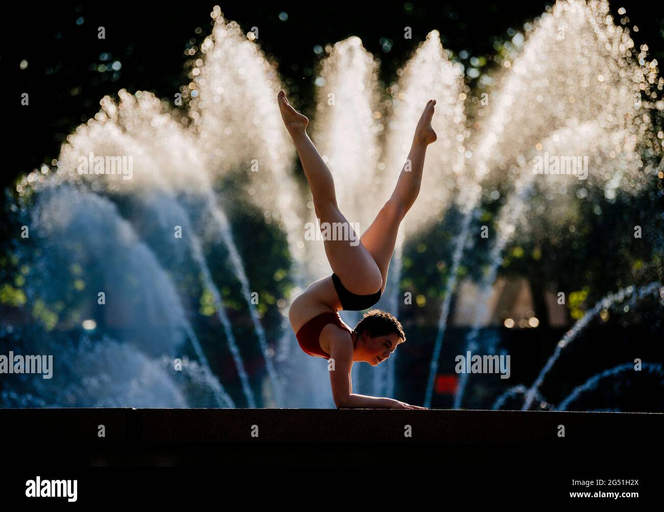 Woman doing acrobatic handstand pose against fountain Stock Photo