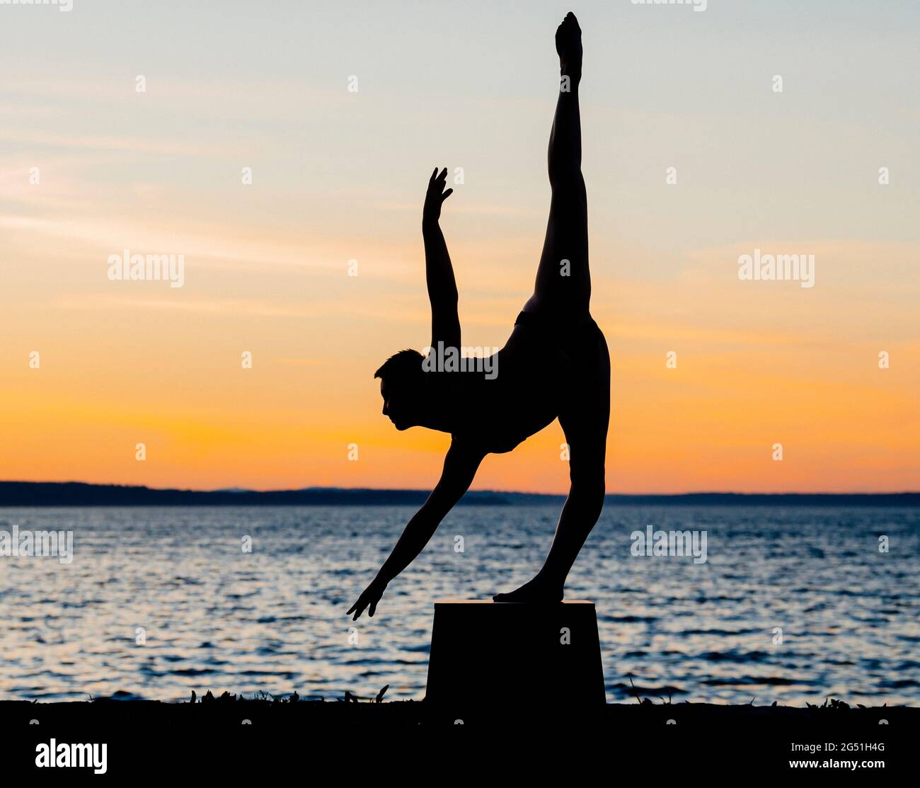 Silhouette of woman doing acrobatic pose against sea at sunset Stock Photo