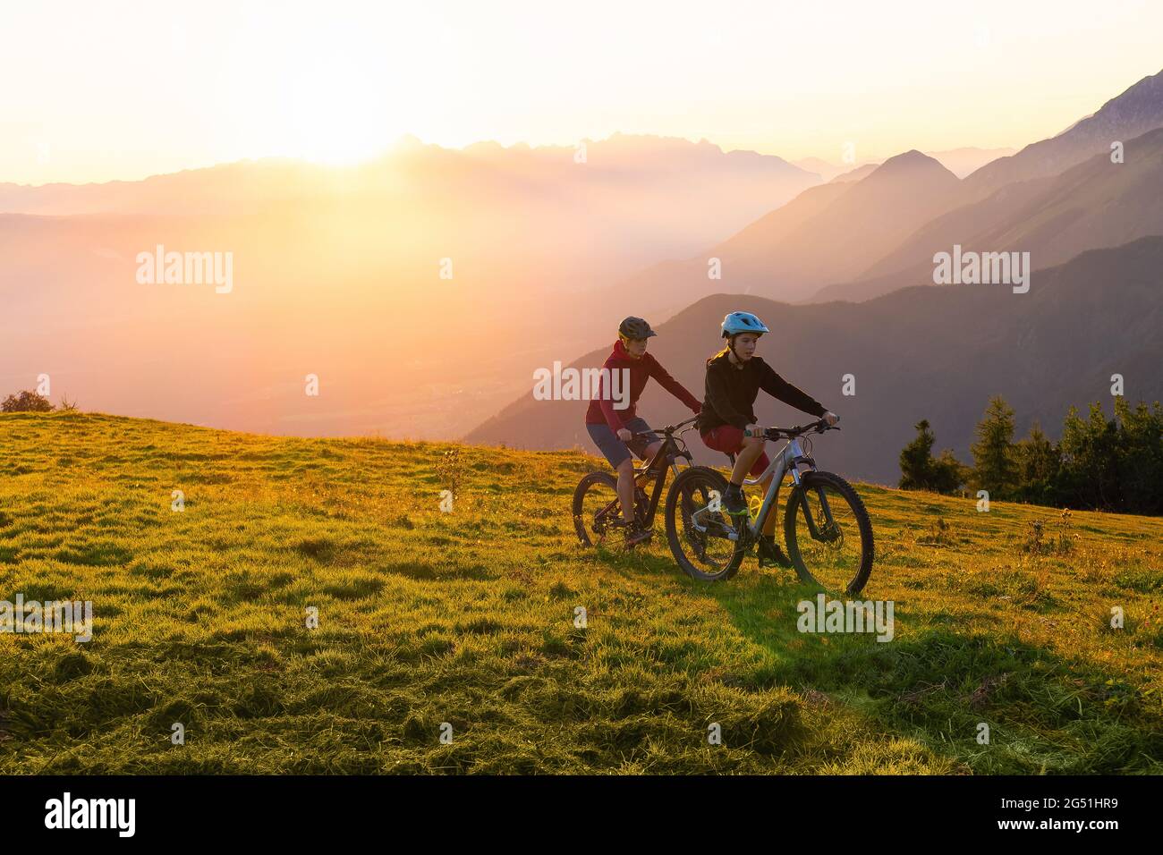 Mother and daughter cycling on mountain bikes at a sunset in mountains. Stock Photo