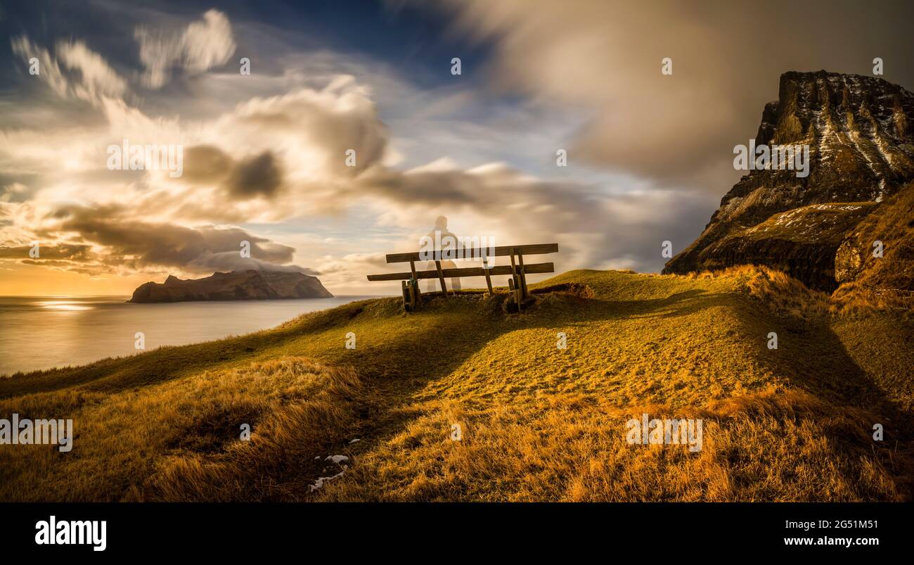 Bench on cliff at sunset and Mykines island in background, Faroe Islands, Denmark Stock Photo