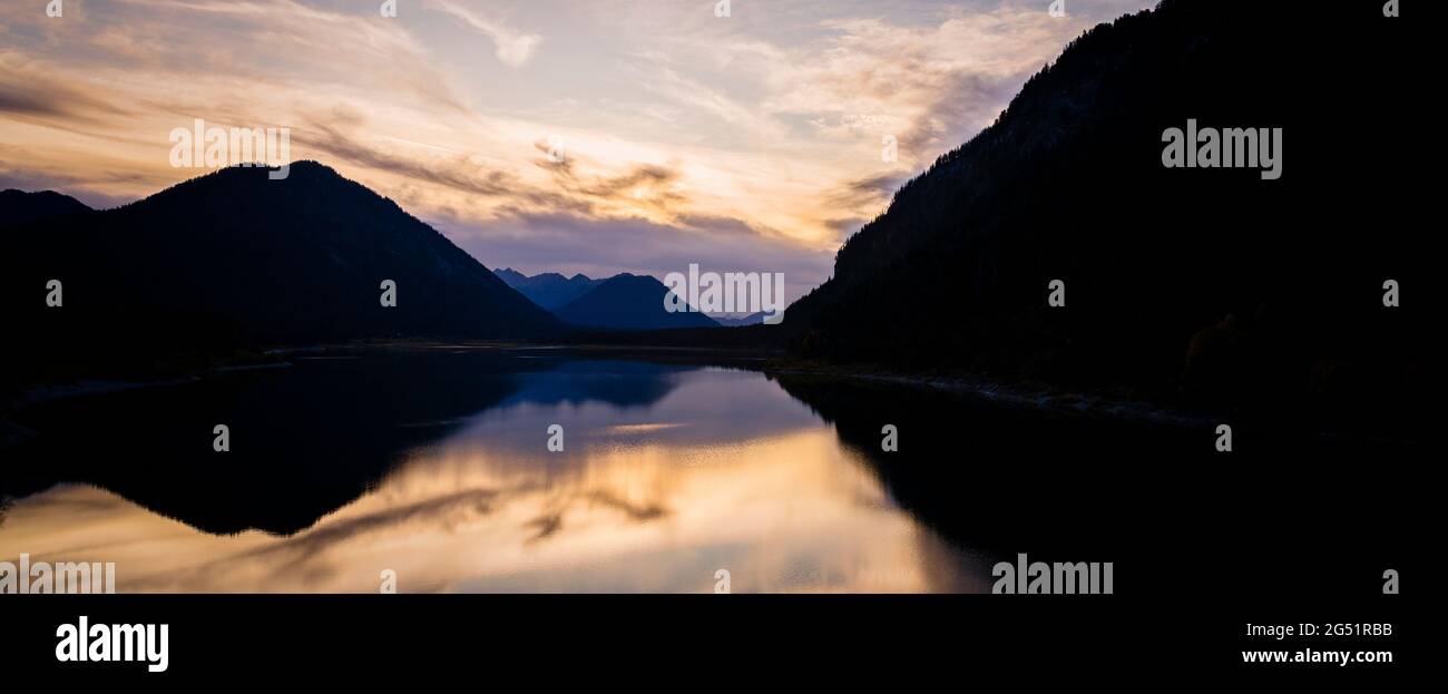 Silhouetted mountains reflecting in Sylvenstein Lake at sunset, Bavaria, Germany Stock Photo