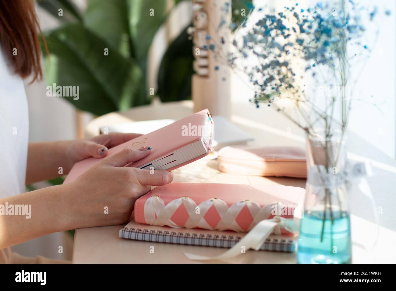 Female hands holding pink coral coloured leather diary 2021 while sitting near a window at cafe Stock Photo