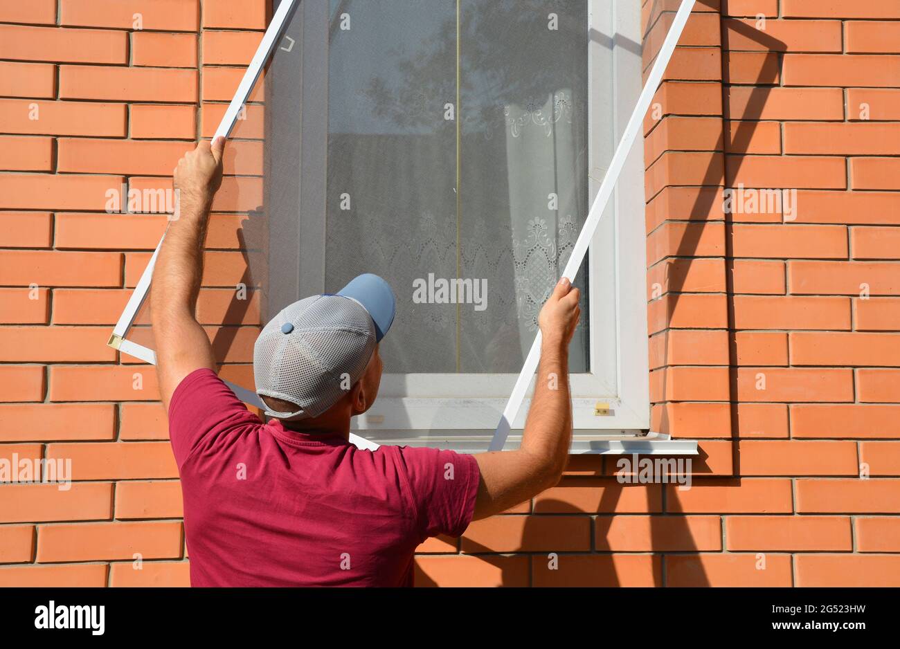 A man is installing a mosquito, insect window screen, net on a house window to prevent mosquitoes and flies from getting inside the house. Stock Photo