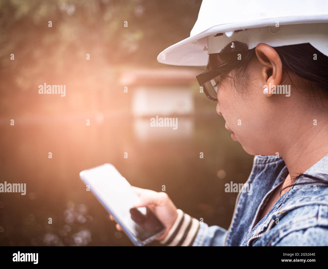 Female ecologist in safety hat working with a smart phone and controlling a quality of water at wastewater treatment plant. Environmental engineers wo Stock Photo