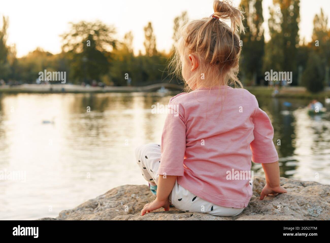 Little girl sitting on a huge stone in park near the lake Stock Photo ...