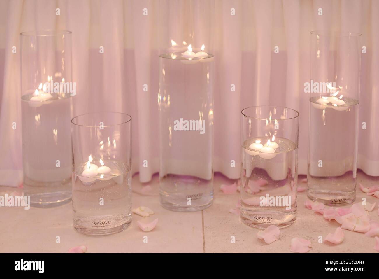 Candles burning in water in candlesticks on pink background surrounded