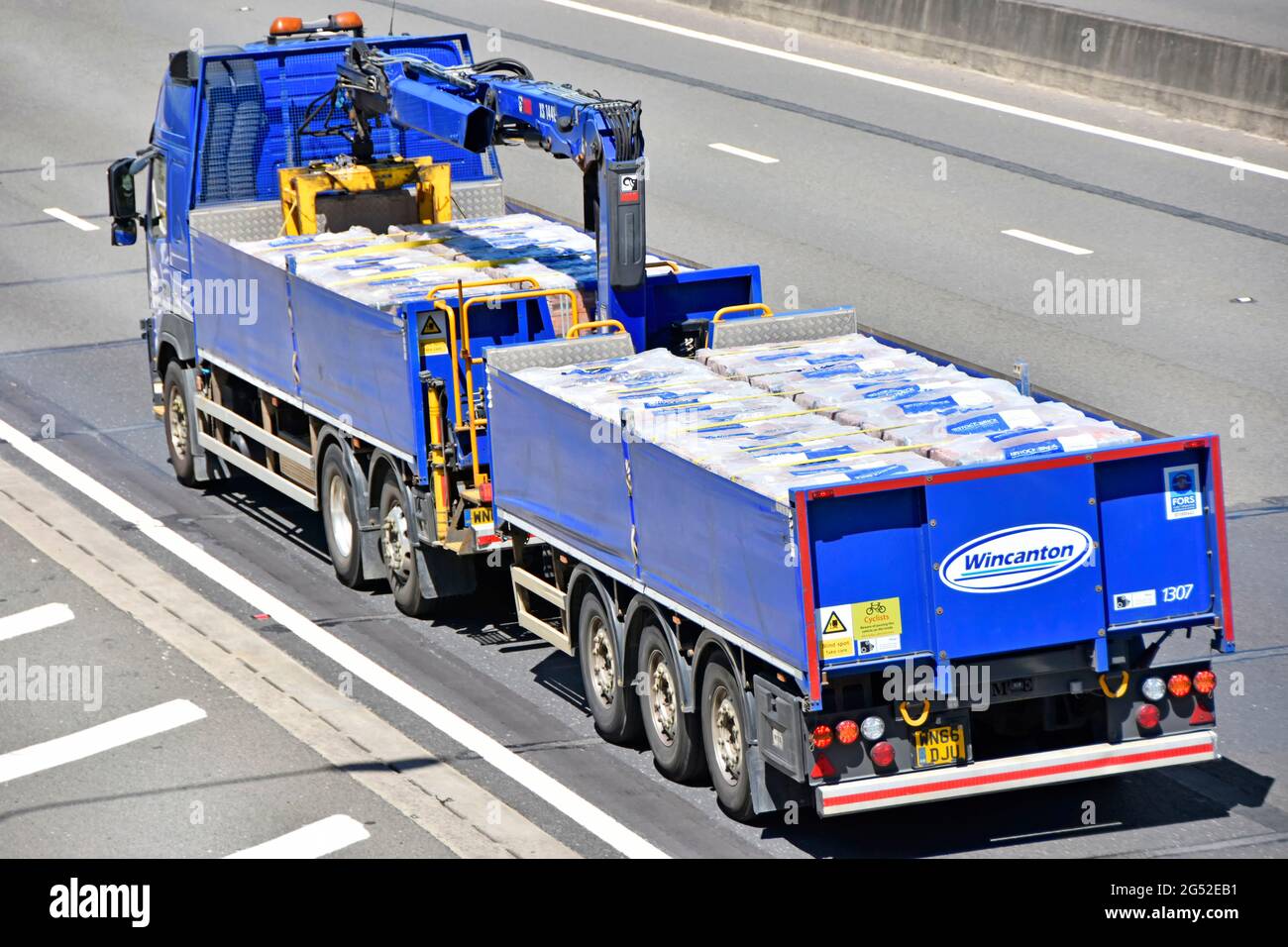Wincanton logistics business lorry truck towing trailer delivering packs of building bricks to UK construction industry sites built in hydraulic crane Stock Photo