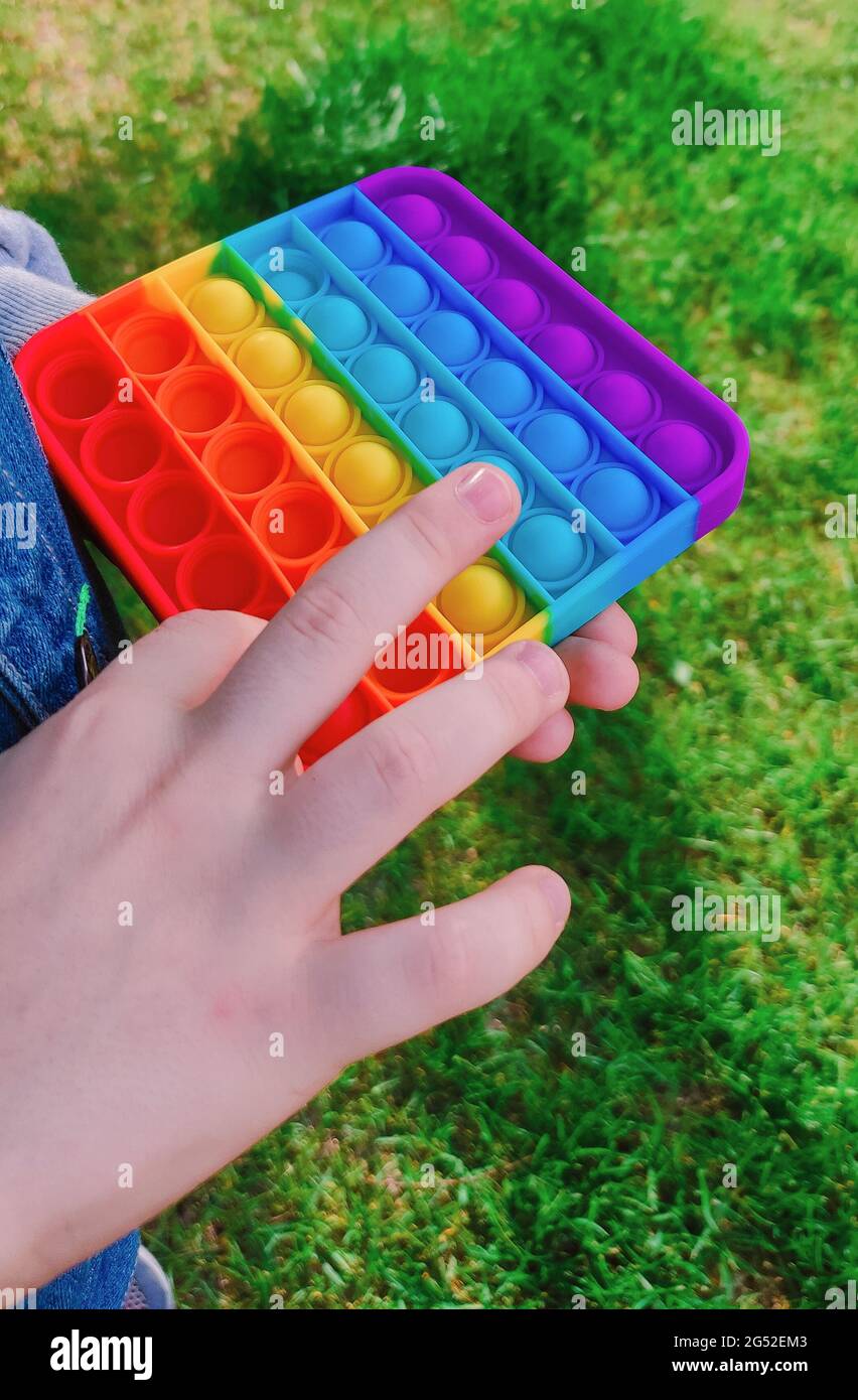 Trendy relaxing toy pop-it in boy's hands. A kid is holding anti stress fidget toy popit. Popular game for adults and children. High quality photo Stock Photo