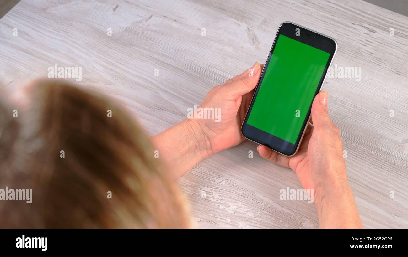 Middle-aged female senora uses an iPhone smartphone with a chroma key screen, copy space, top view. Online shopping concept, use of mobile Stock Photo