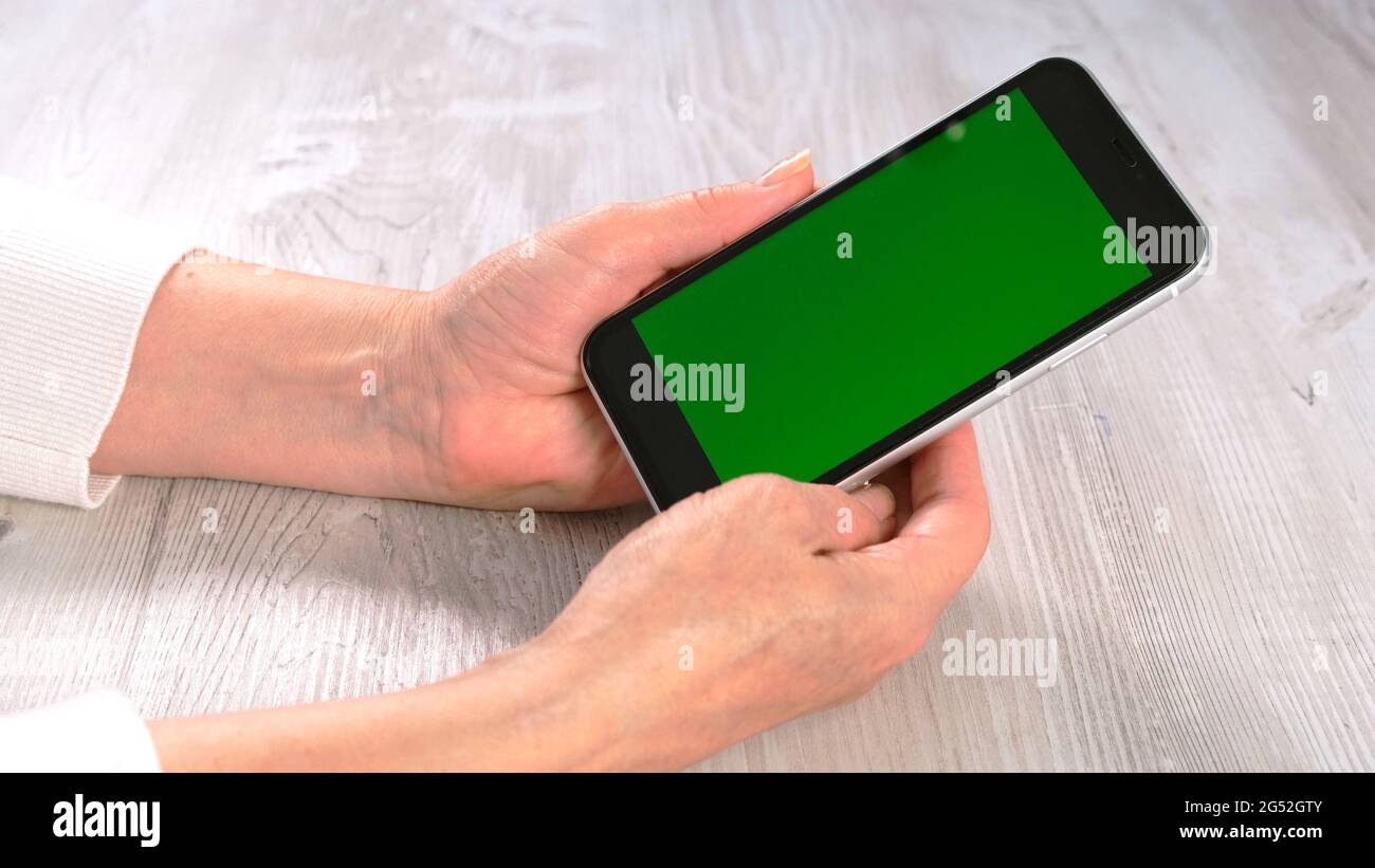 Hands of a middle-aged woman senior uses a smartphone iPhone with a chroma key screen, copy space. Online shopping concept, use of mobile applications Stock Photo