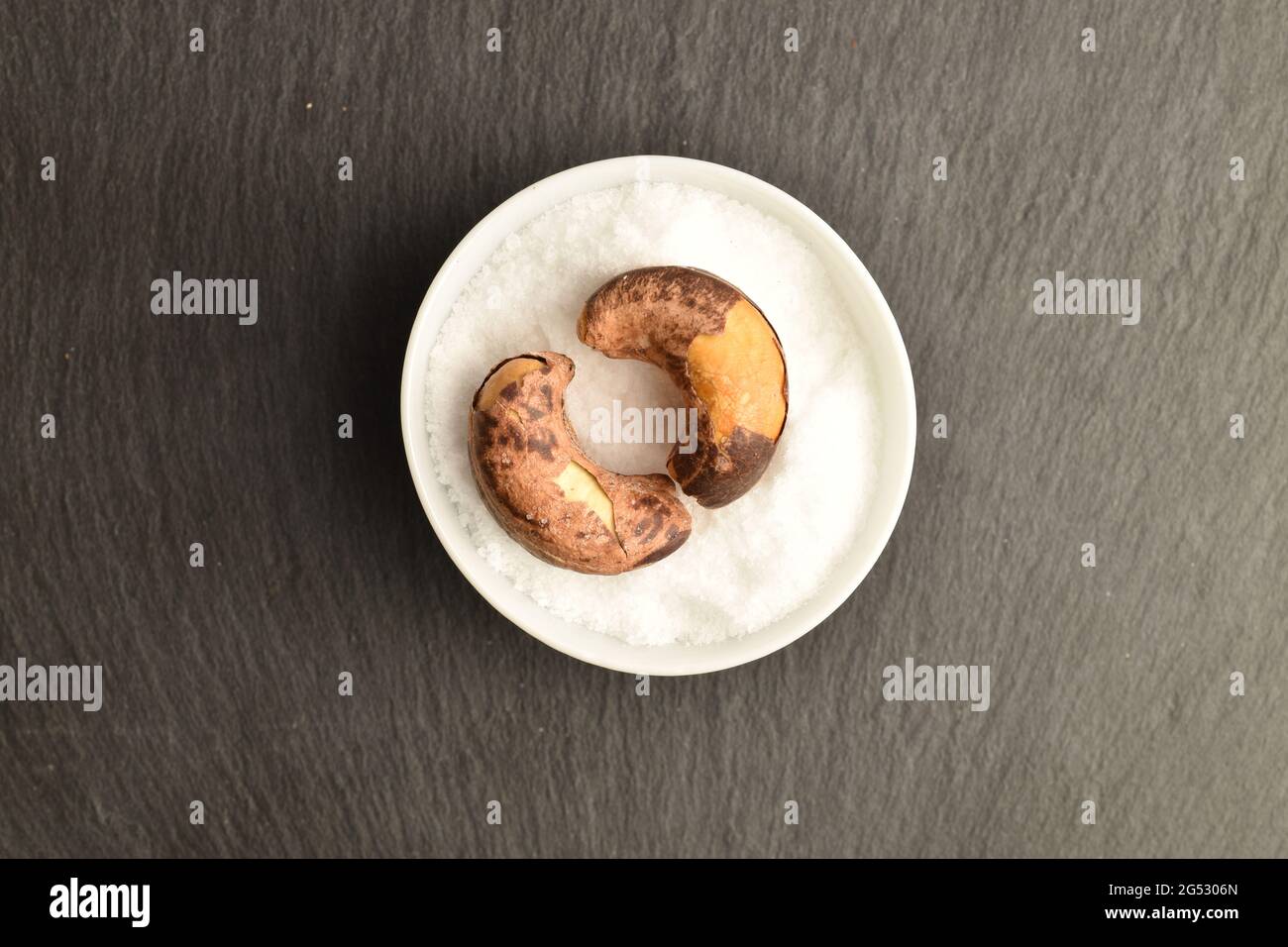 Two roasted cashews in a salt shaker, close-up, on a slate board, top view. Stock Photo