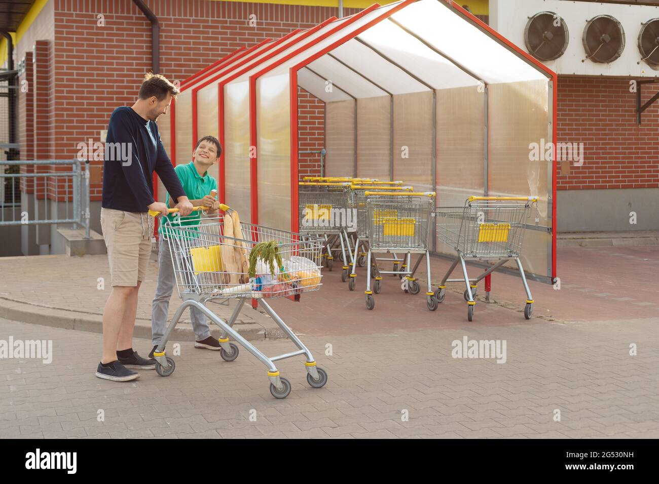 Dad and son went shopping together and walk to car with Shopping Cart ...