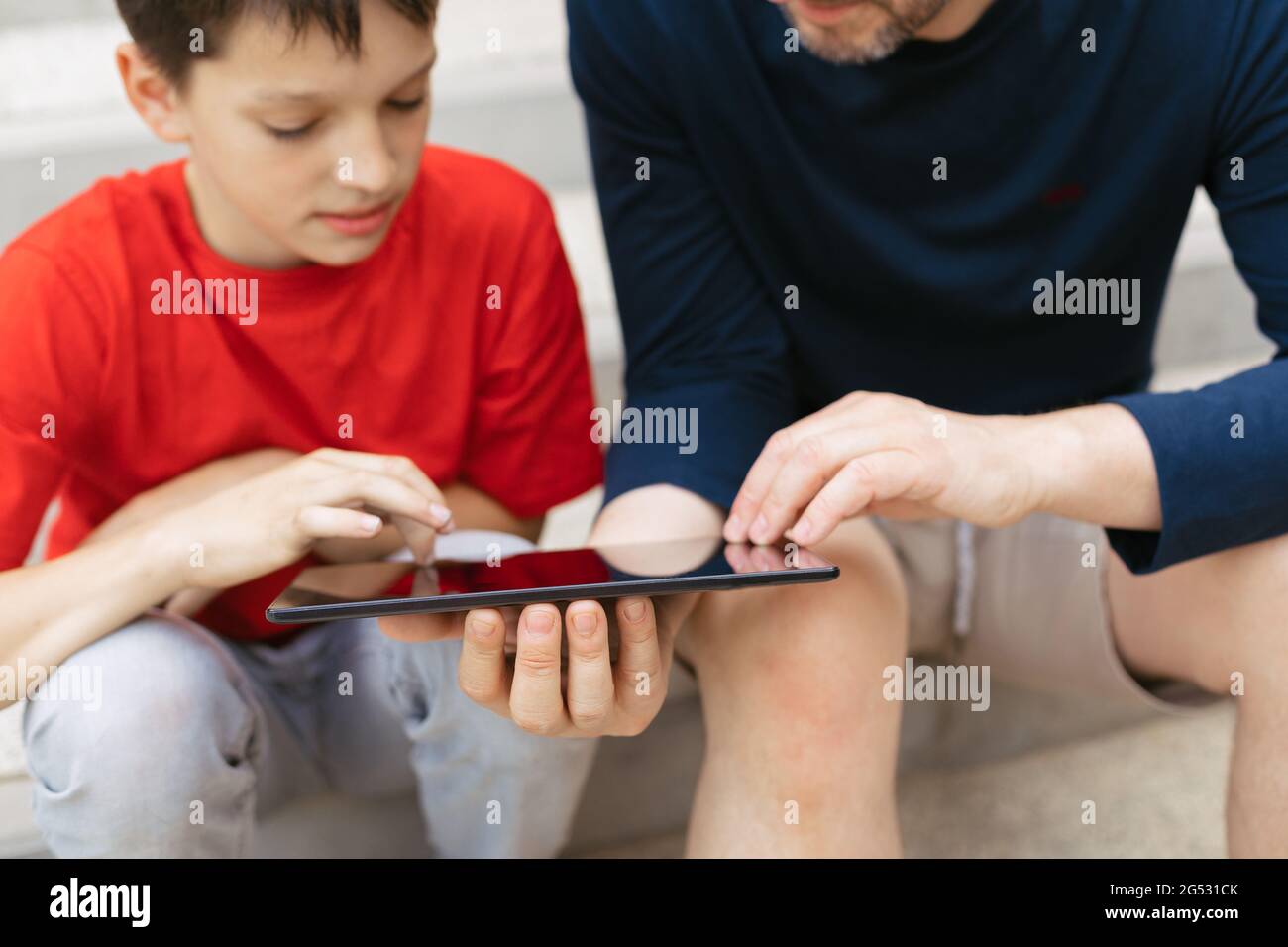 The concept of using gadgets for education or spending time with children. Young dad and son on steps of concrete staircase Stock Photo