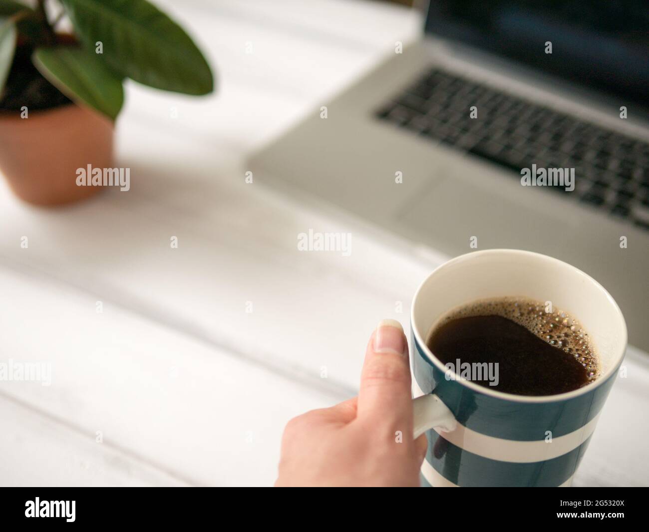 The large mug of coffee in the hand near laptop Stock Photo