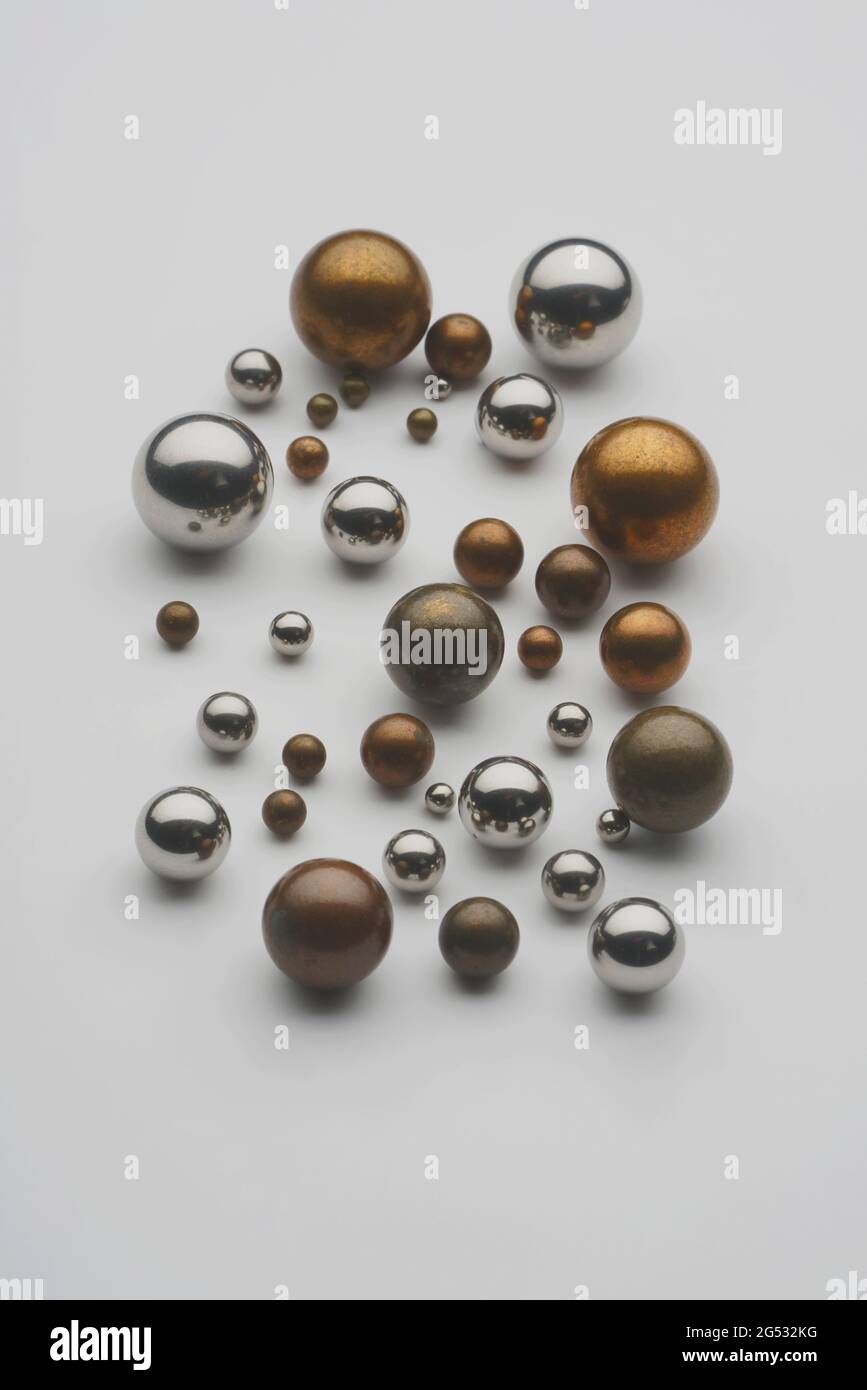 Close up top view showing group of assorted industrial steel, brass, non ferrous metal balls used in bearings arranged on white background. Stock Photo