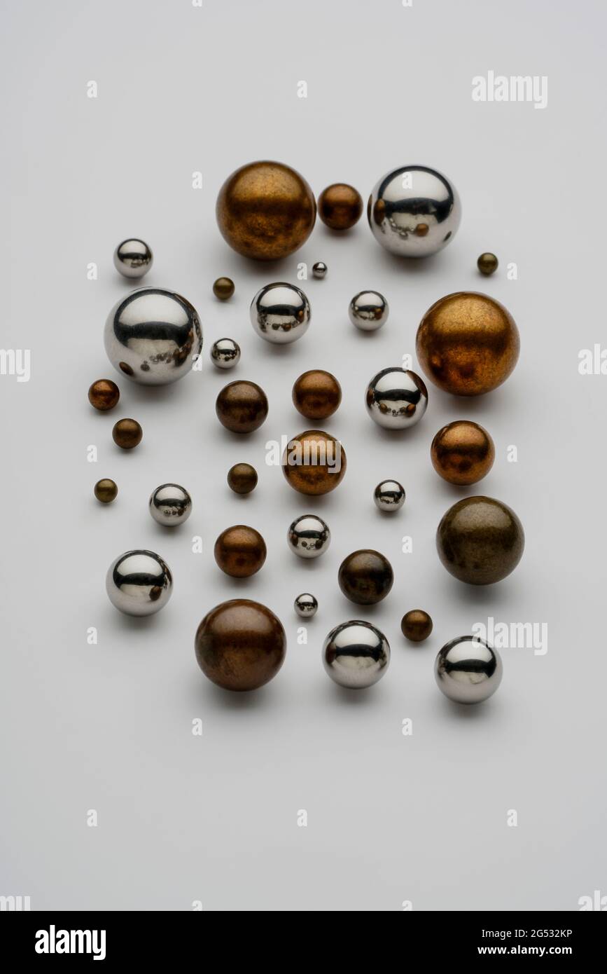 Close up top view showing group of assorted industrial steel, brass, non ferrous metal balls used in bearings arranged on white background. Stock Photo