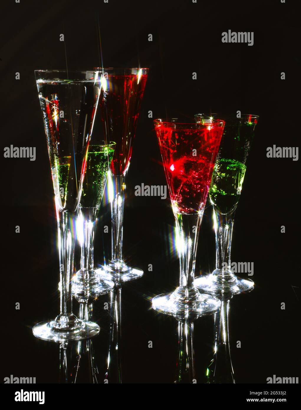 portrait/upright format fluted cocktail glasses containing red and green liquid drinks on black perspex/plexiglass shiny background with starburst Stock Photo