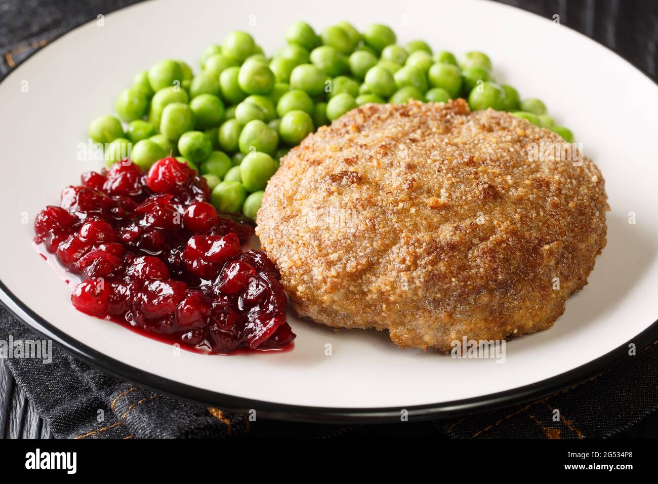 Wallenbergare is a Swedish dish generally consisting of ground veal is traditionally served with boiled green peas closeup in the plate on the table. Stock Photo