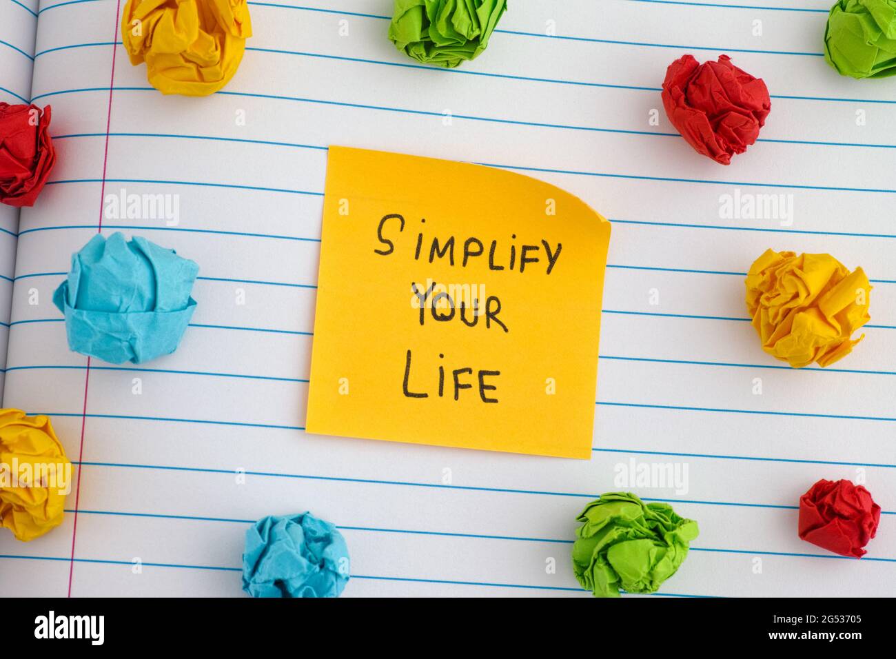 Simplify Your Life. A yellow paper note with the phrase Simplify Your Life on it with some colorful crumpled paper balls around it. Close up. Stock Photo