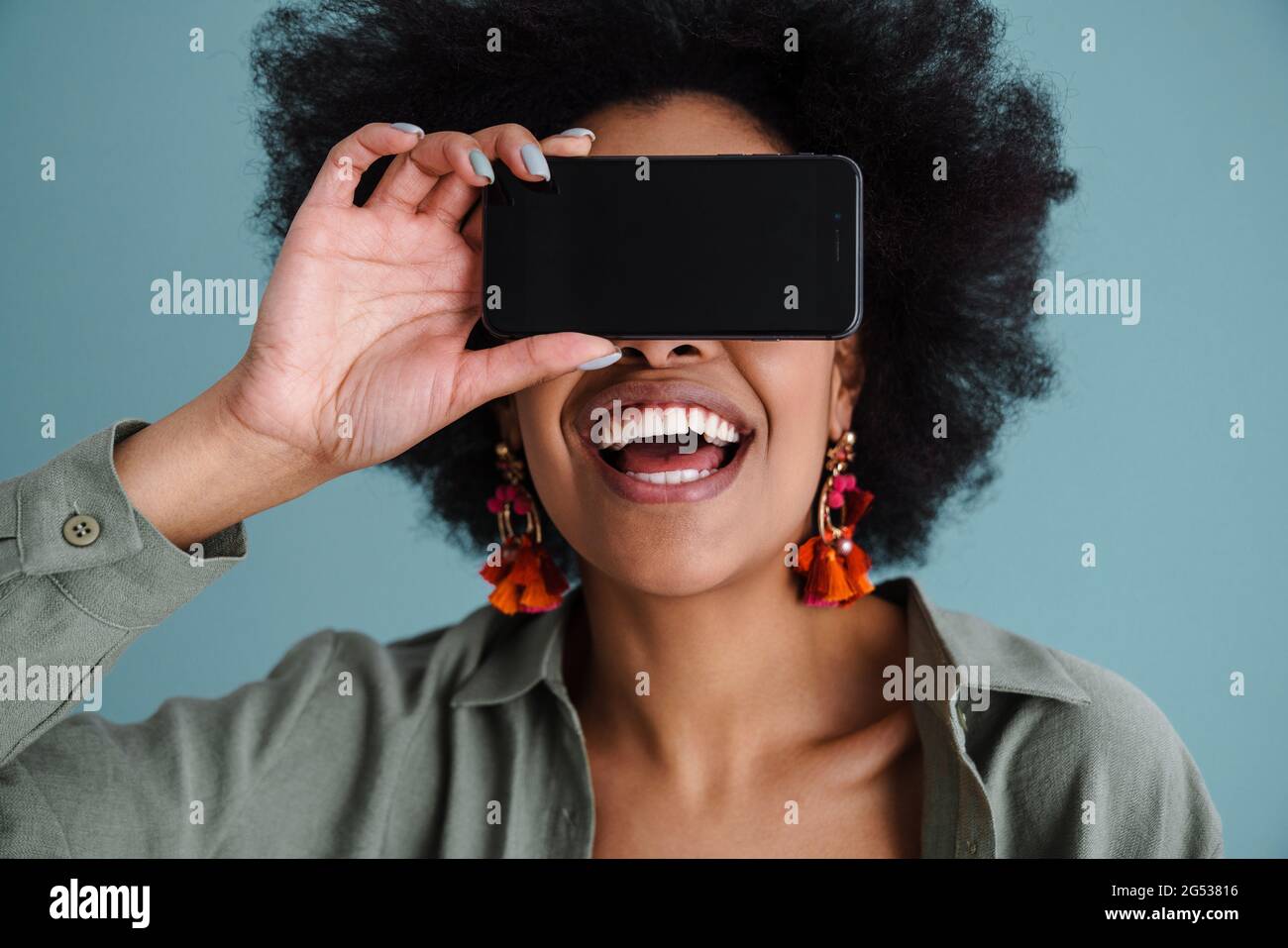 Joyful african american girl making fun with mobile phone isolated over blue background Stock Photo