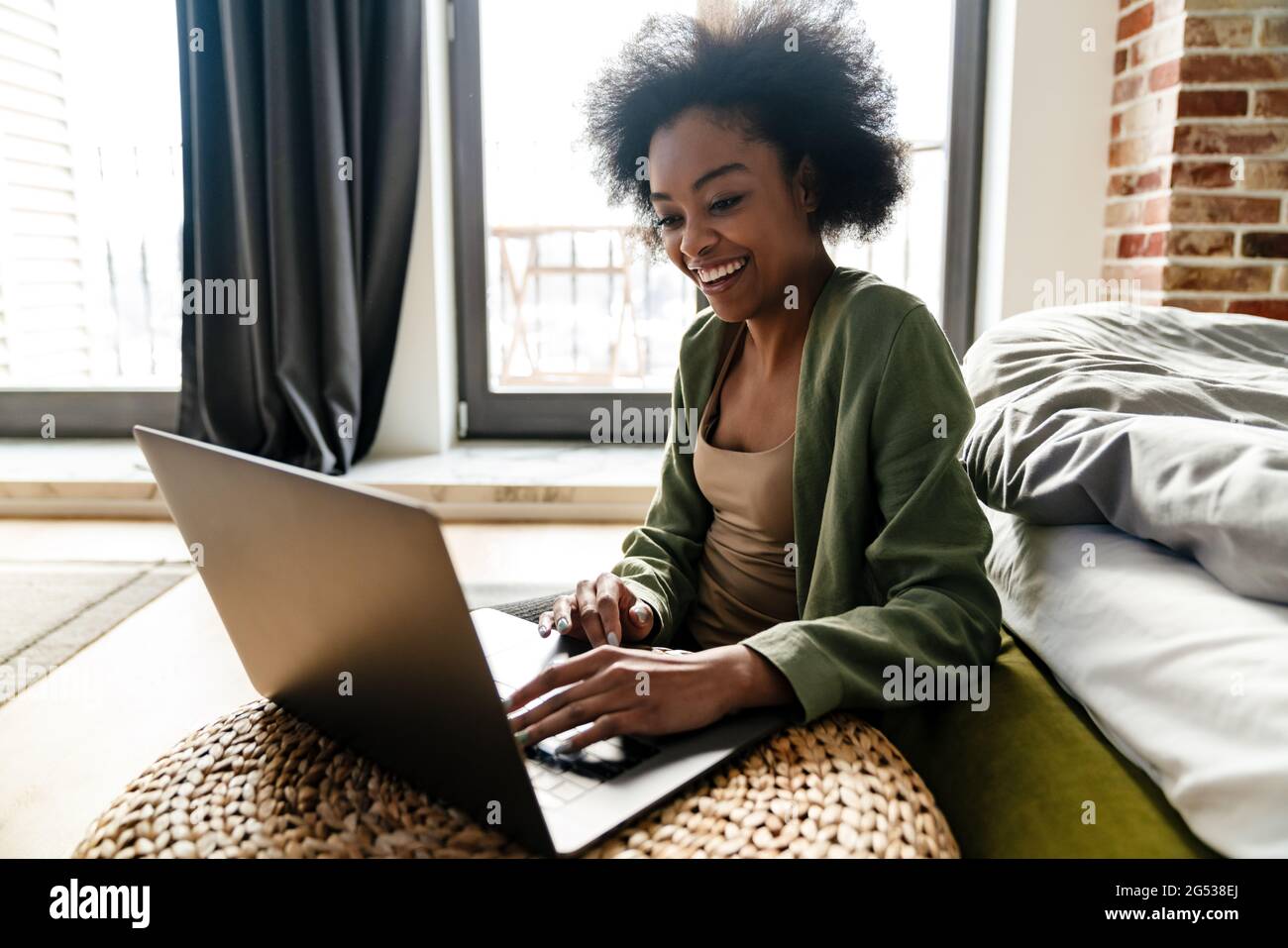 Happy african american girl using laptop while sitting on floor at home ...