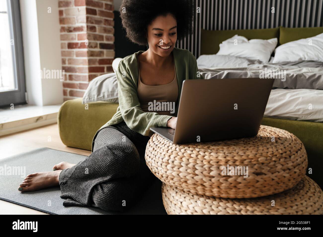 Happy african american girl using laptop while sitting on floor at home ...