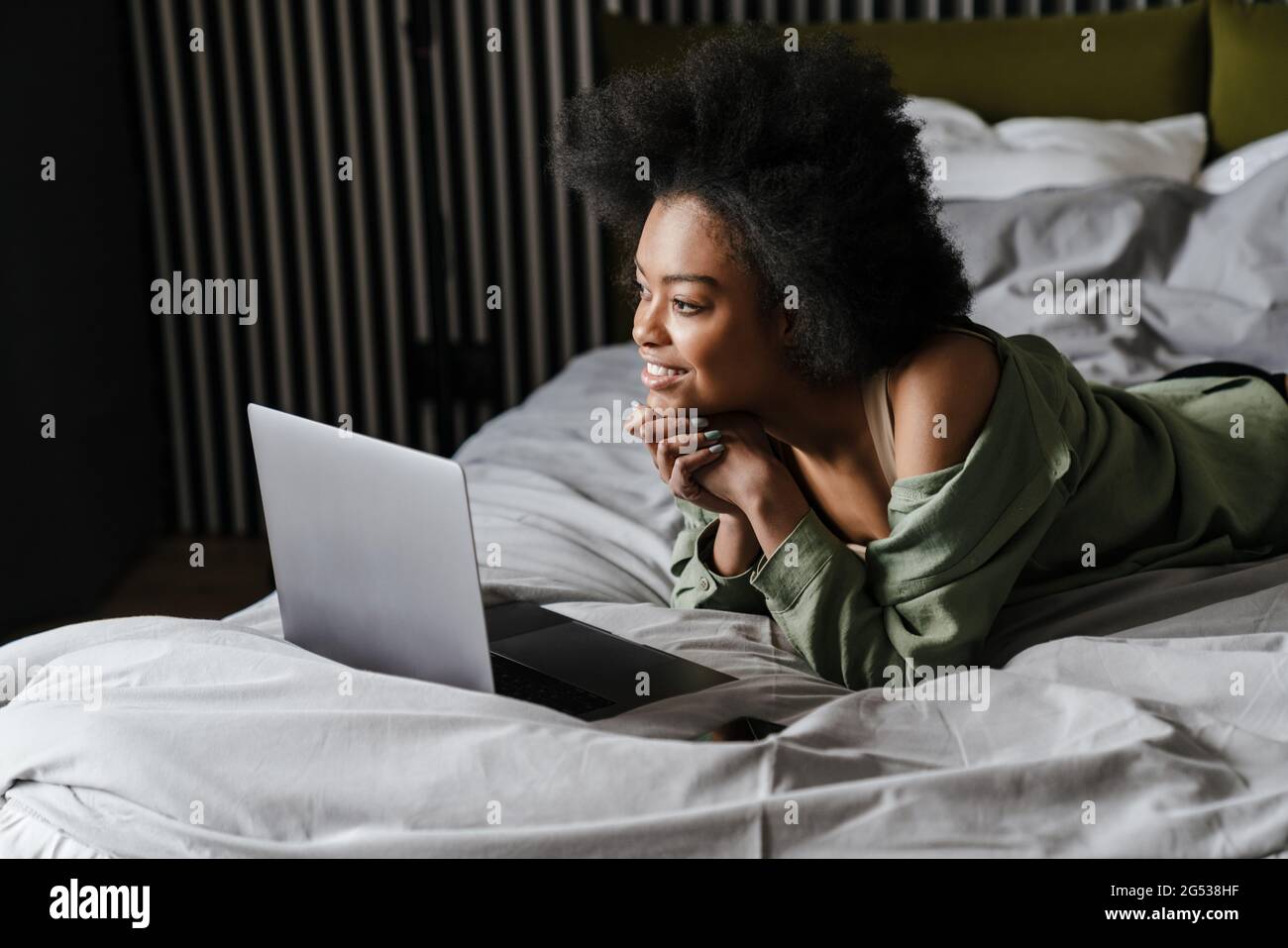 Happy african american girl using laptop while lying in bed after sleep ...