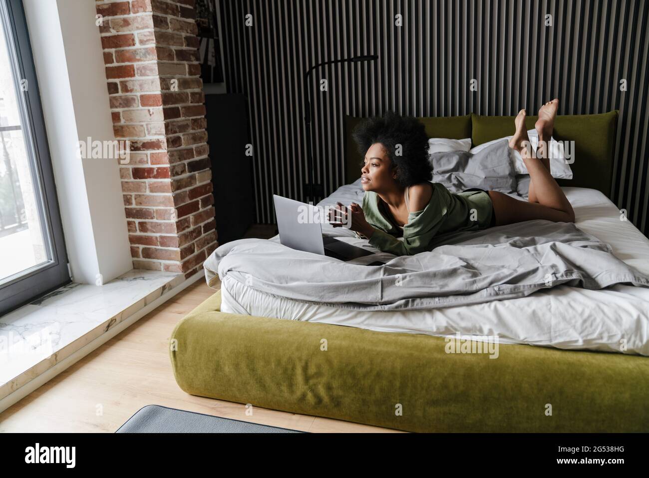 Focused african american girl using laptop while lying in bed after ...