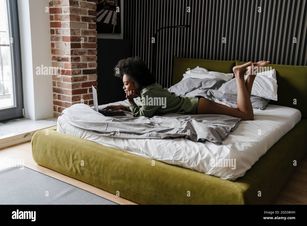 Focused african american girl using laptop while lying in bed after ...