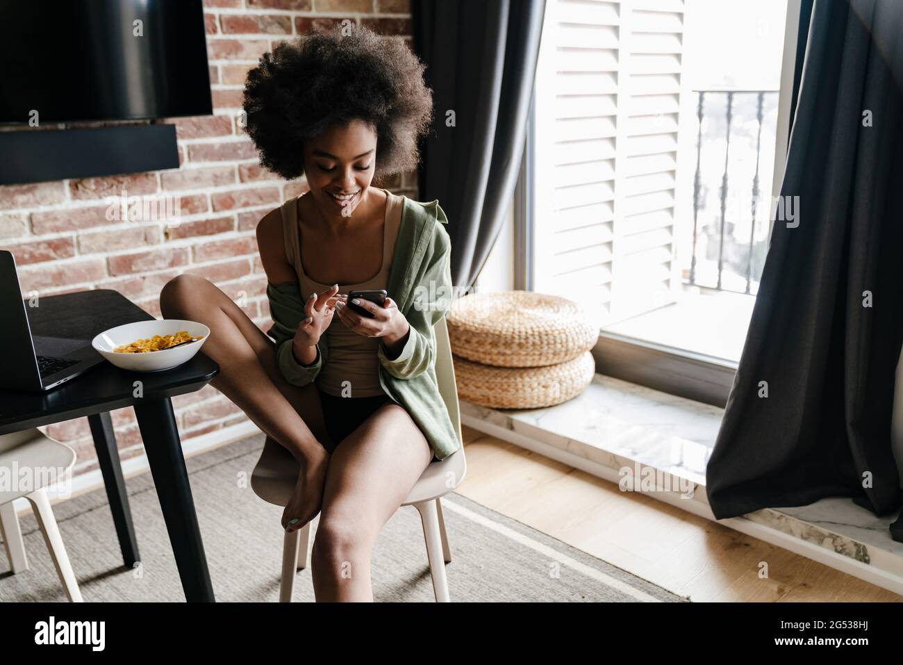 Happy african american girl using mobile phone while sitting at home ...