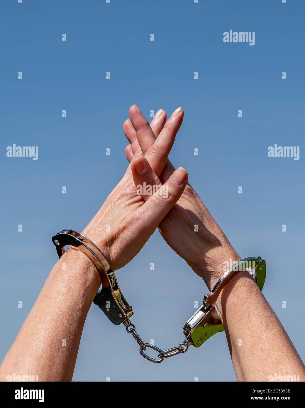 A woman holds her arms up to the sky with her hands bound by iron handcuffs Stock Photo