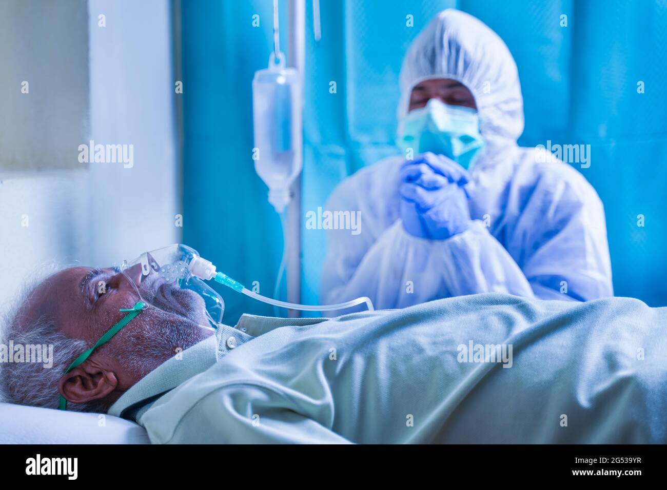 Worried family member or doctor in PPE or protective suit praying for coronavirus or covid-19 infected patient for recovery at hospital while patient Stock Photo