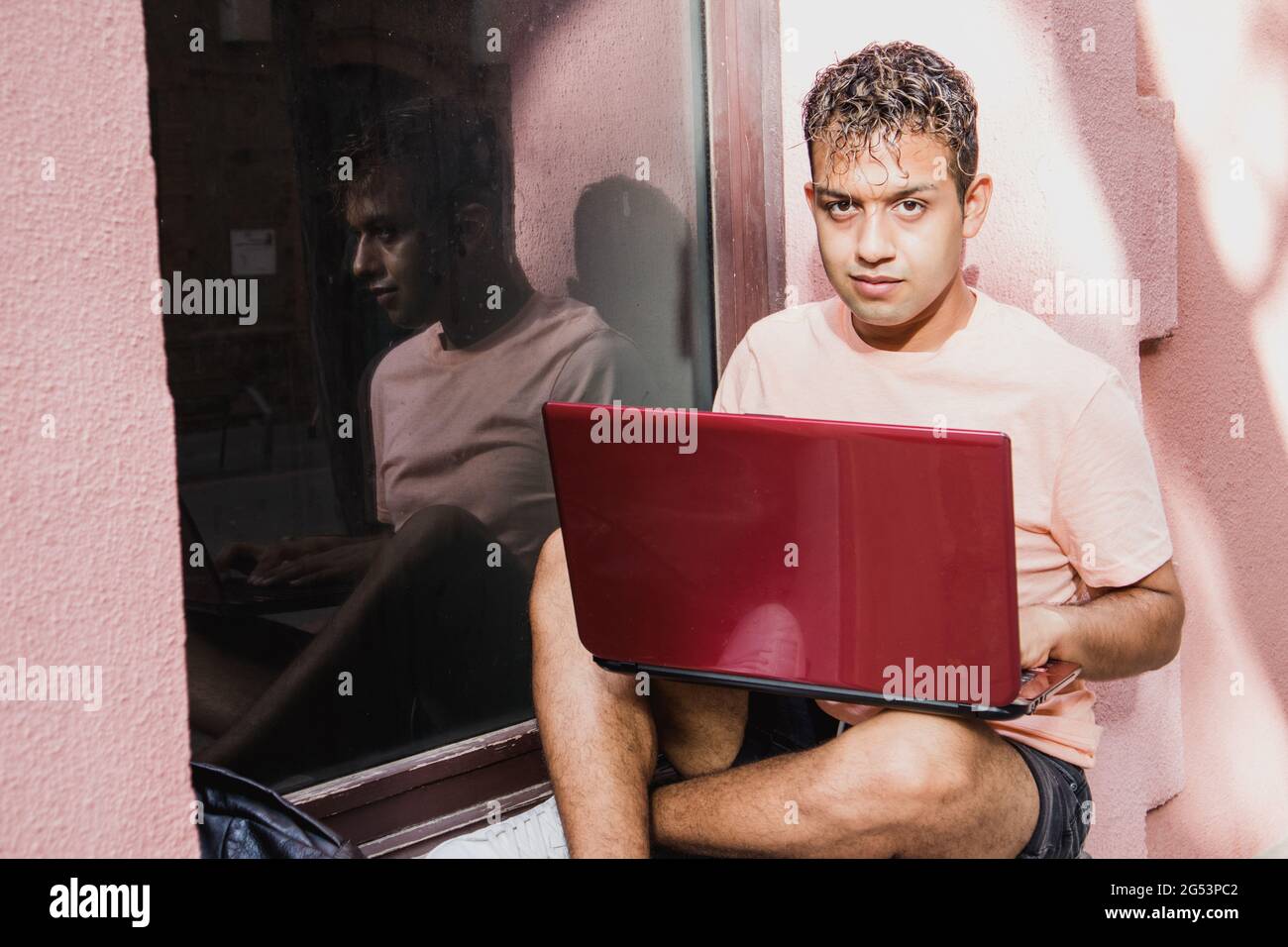 Hispanic boy with laptop. Latino young man working with computer and looking at camera. Stock Photo