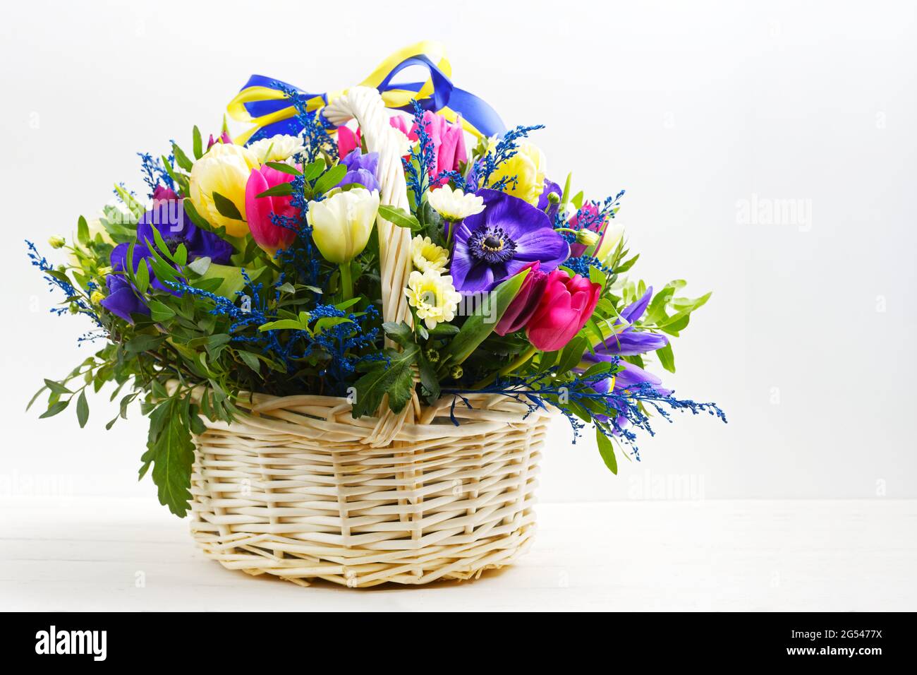 Bouquet of flowers in a wicker basket on white wooden table Stock Photo