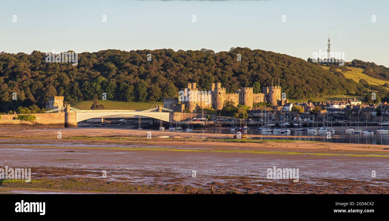 Looking across the River Conwy at Conwy Castle during sunset with the metal train line tunnel visible in the scene. Stock Photo