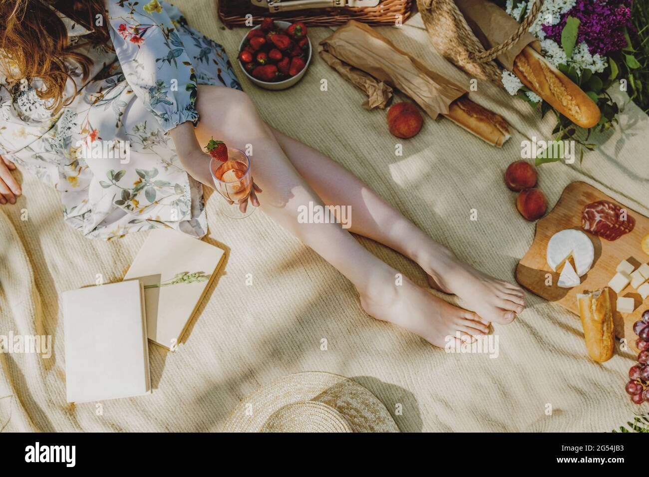 Beautiful legs of young woman in white sitting on blanket and having picnic. Stock Photo