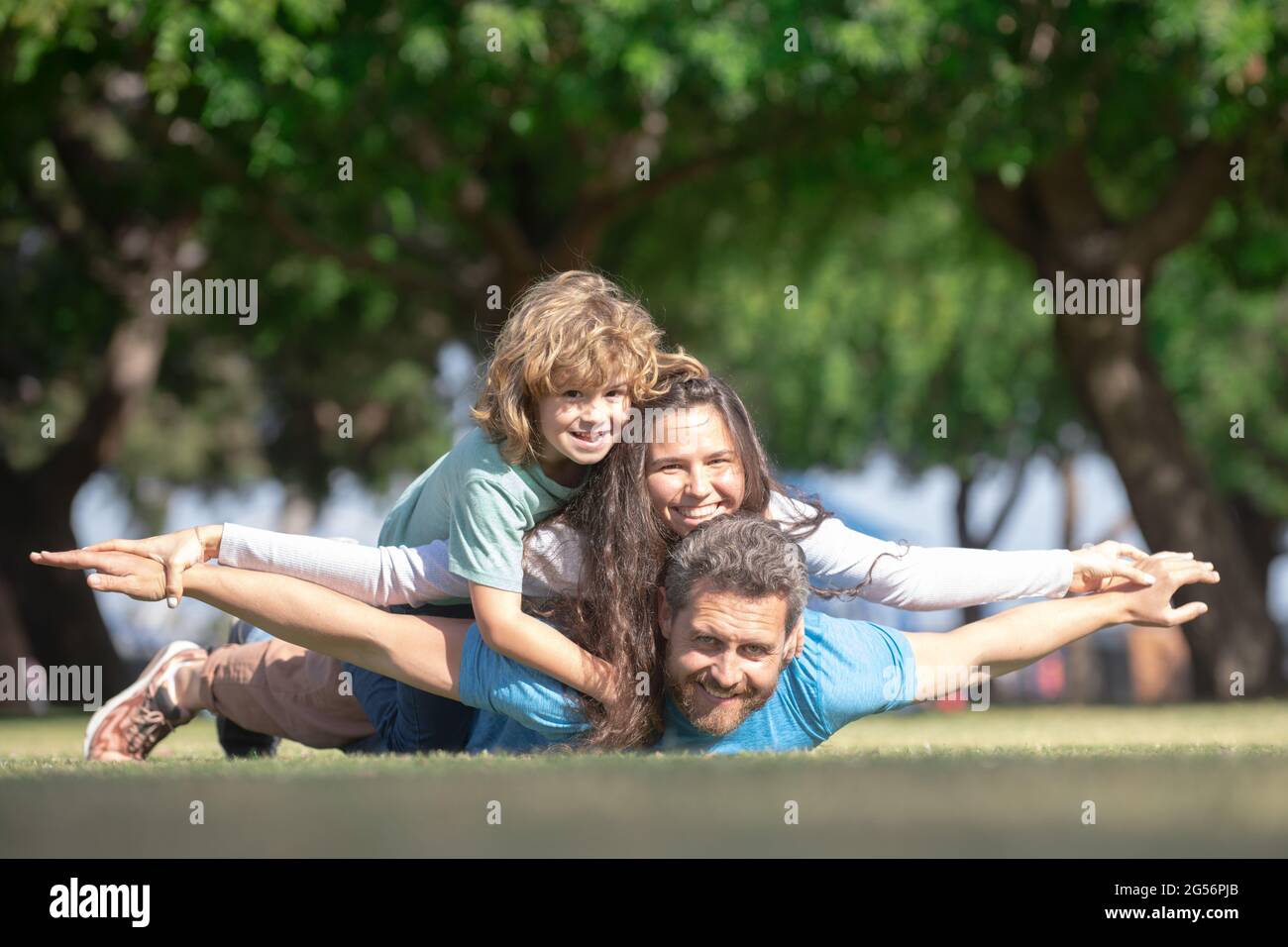 Mother father and child son hugging and embracing outdoors at summer park. Fly concept, little boy is sitting pickaback while imitating the flight. Stock Photo