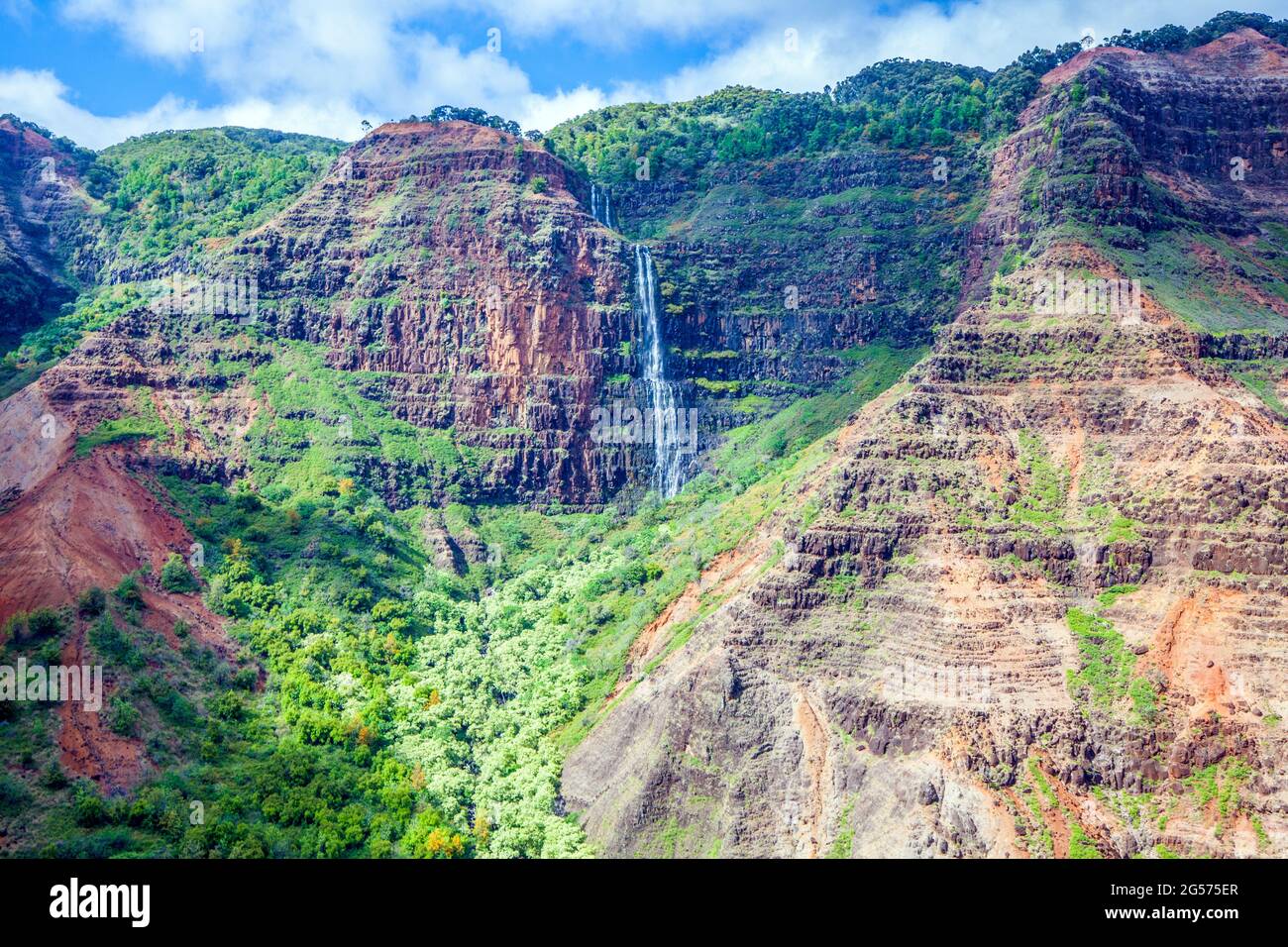 A waterfall flows down Kauai's Waimea Canyon near the Napali Coast; Kauai, Hawaii Stock Photo