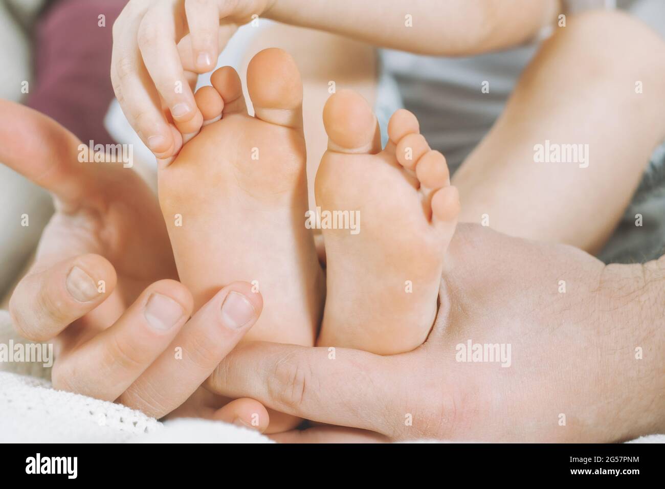 Children's feet in hands of father. Dad tickles feet of kid. Baby counts toes Stock Photo